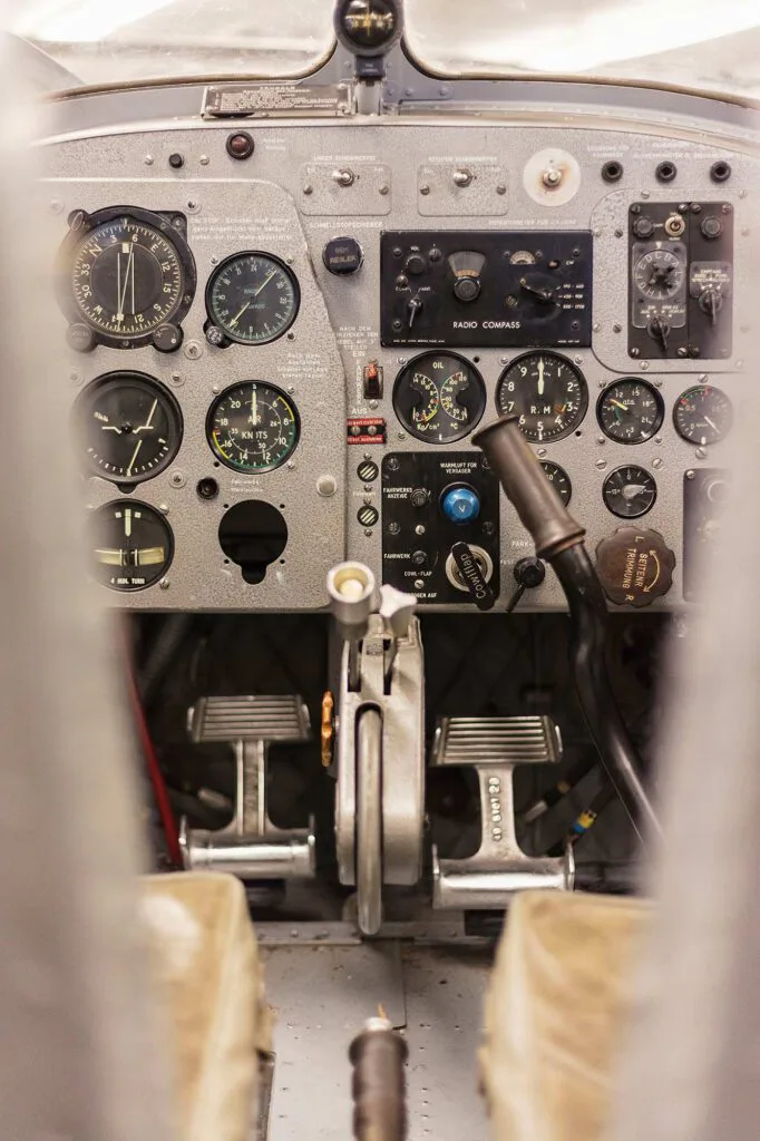 Blick in ein Flugzeugcockpit mit analogen Instrumenten, Steuerknüppel und Pedalen zwischen zwei Sitzen.
