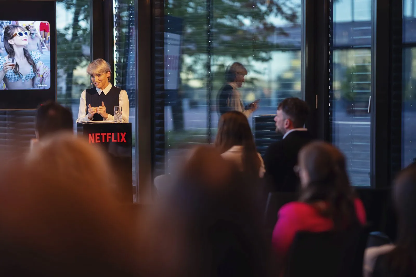 Eine Frau spricht am Netflix-Rednerpult vor sitzenden Gästen in einem Raum mit großen Fenstern.