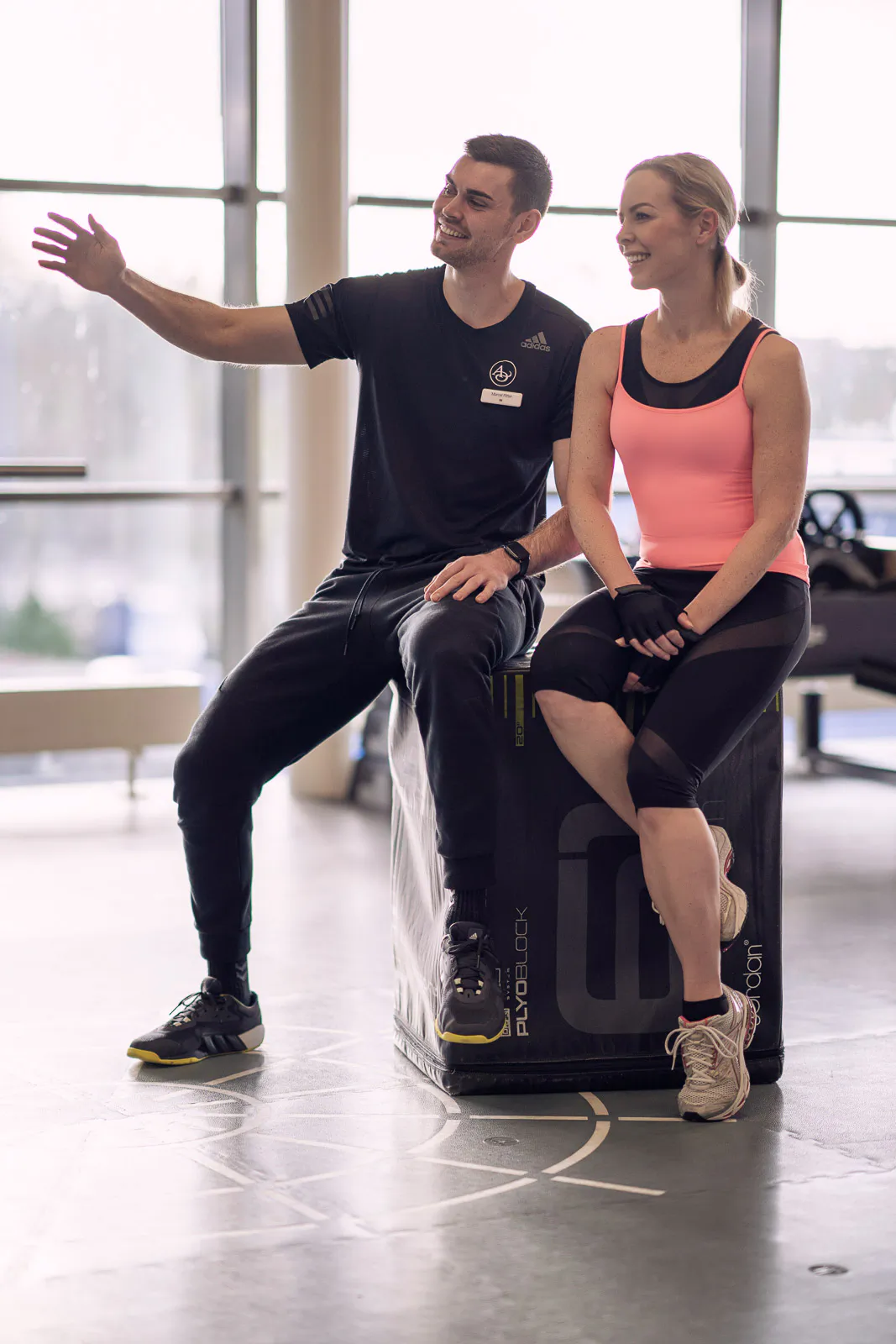 Isabel Edvardsson und ein Mann sitzen in Sportkleidung auf einer Trainingsbox vor hellen Fenstern. Er gestikuliert.