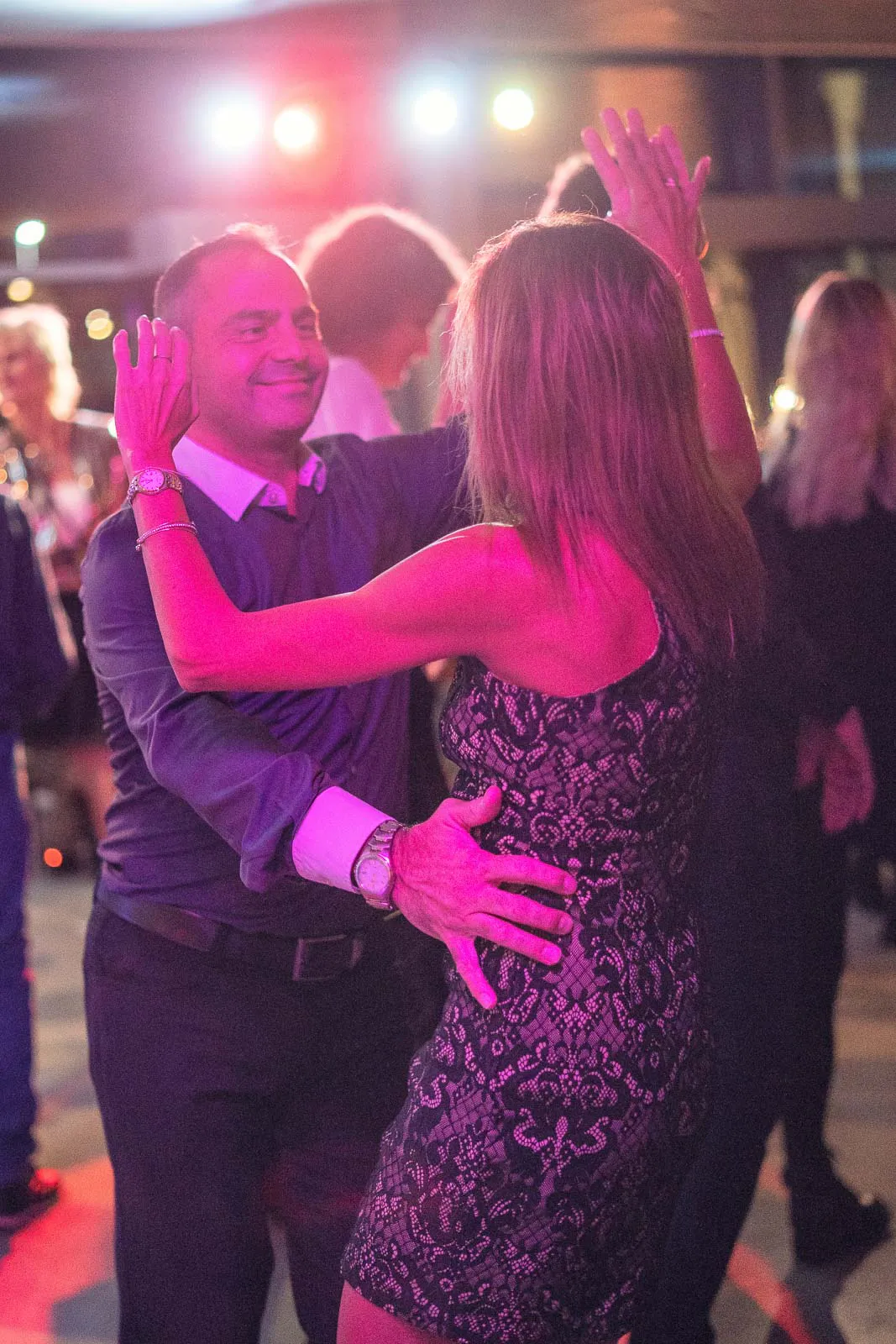 Ein Mann und eine Frau im schwarzen Spitzenkleid tanzen bei pinkem Licht zwischen Gästen auf einem Aspria-Event.
