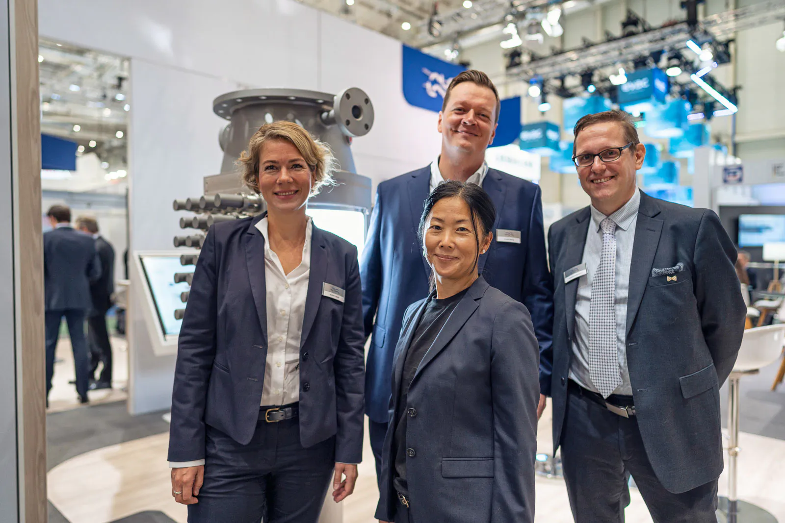 Vier Personen in Anzügen posieren am hell beleuchteten Alfa-Laval-Messestand vor einer Industrieanlage.