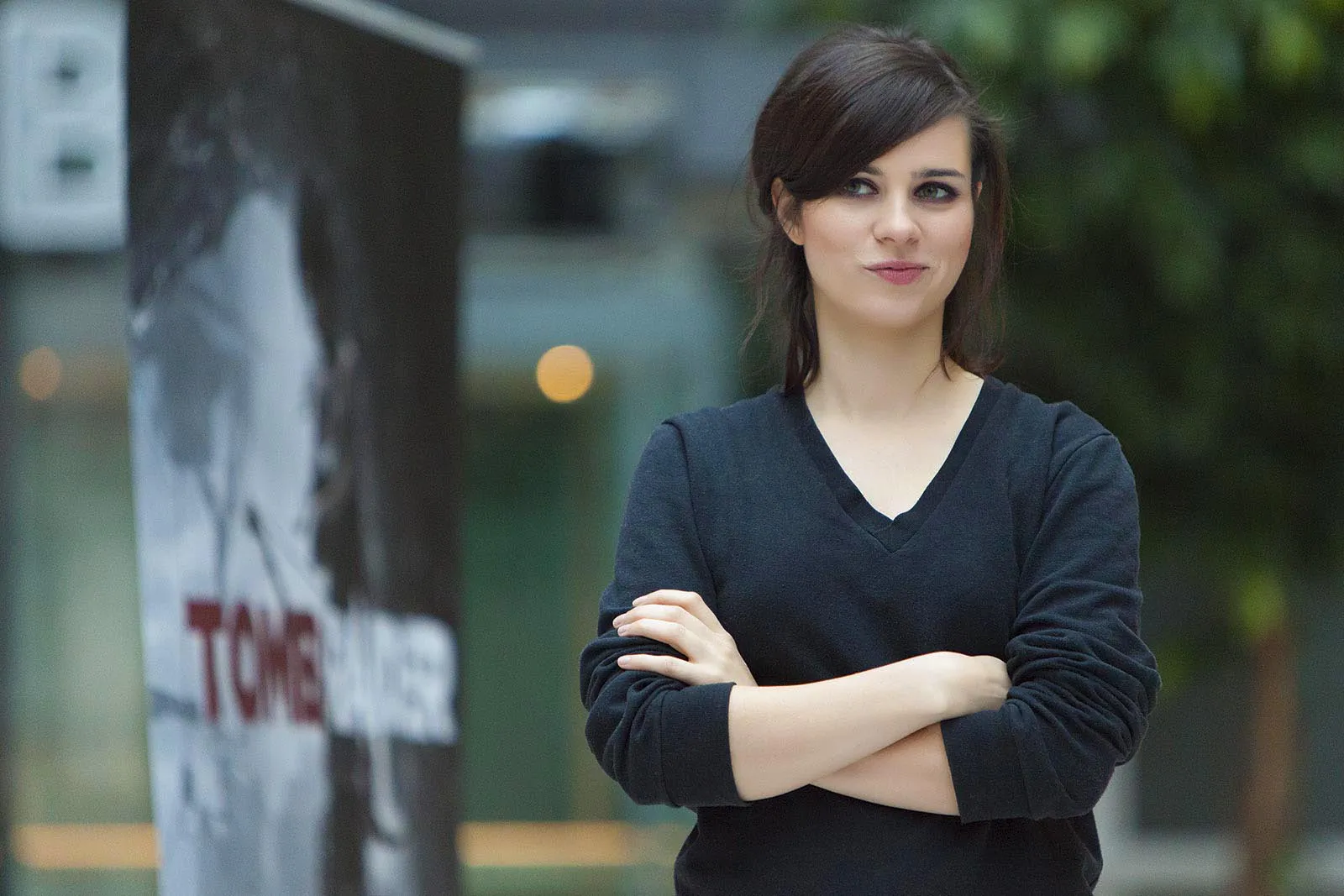 Nora Tschirner steht mit verschränkten Armen im schwarzen Pullover neben einem Tomb-Raider-Aufsteller.