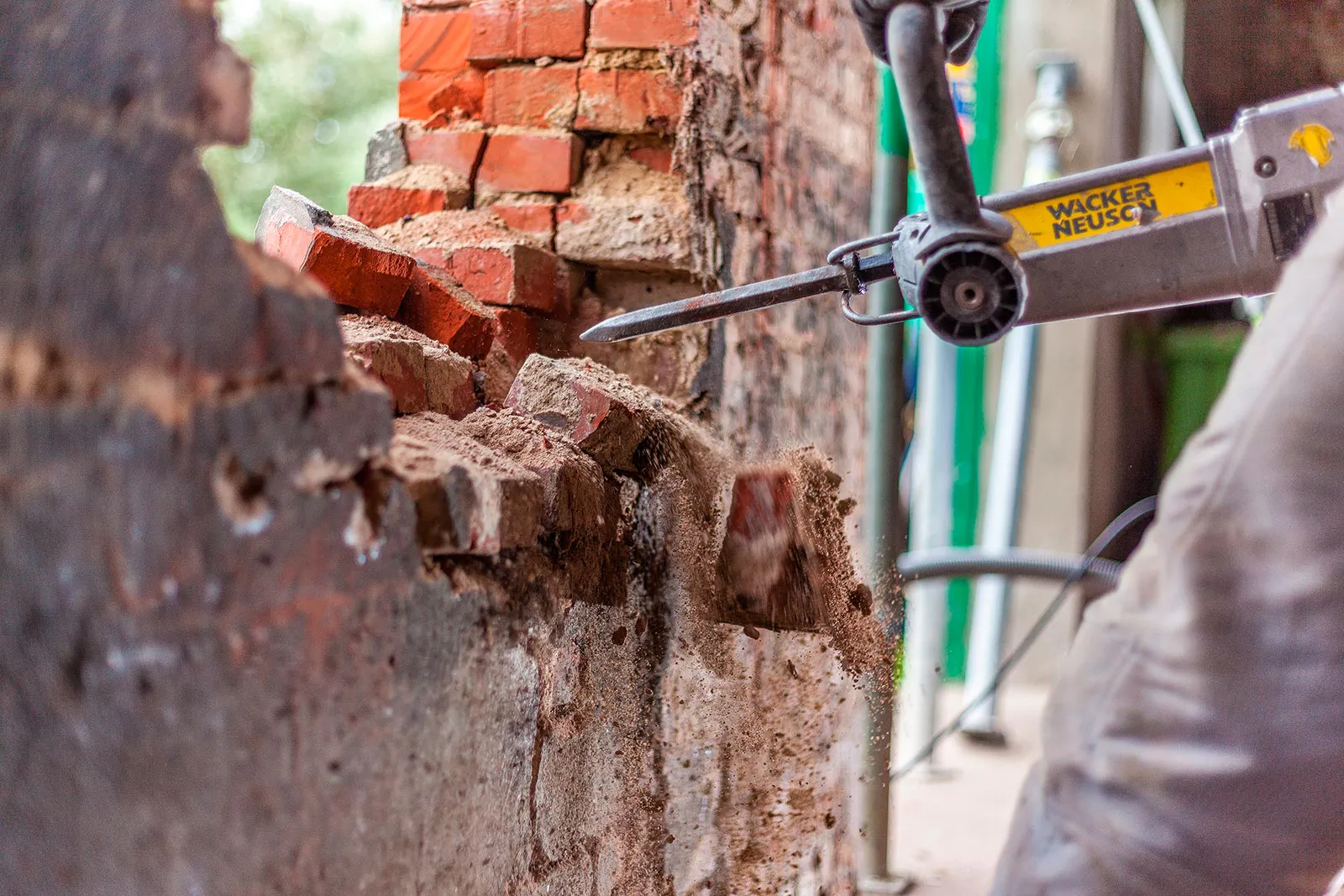 Arbeiter trägt mit einem elektrischen Abbruchhammer eine rote Ziegelwand auf einer Baustelle ab.