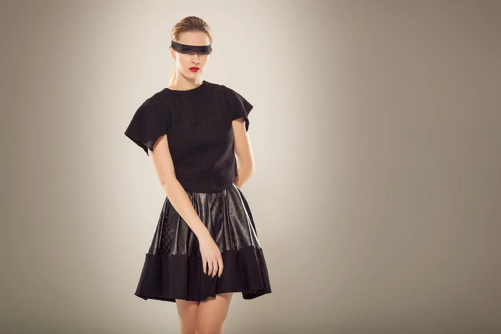 Model mit schwarzer Sonnenbrille, schwarzem Oberteil und glänzendem Rock posiert im weich beleuchteten Studio.