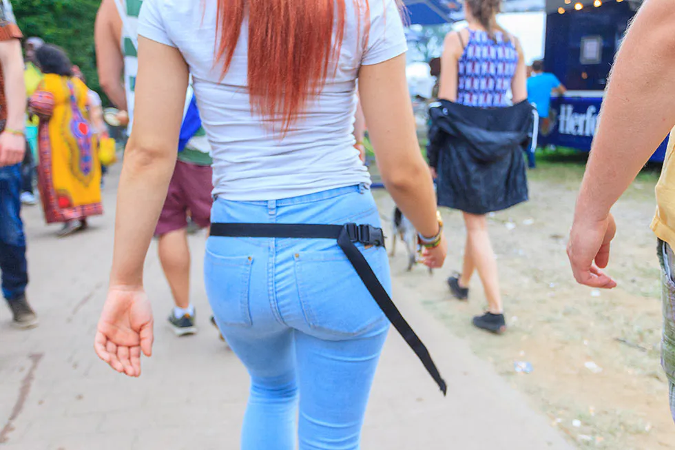 Festivalbesucherin mit langen roten Haaren, weißem T-Shirt und hellblauer Jeans geht zwischen Menschen zur Bühne.