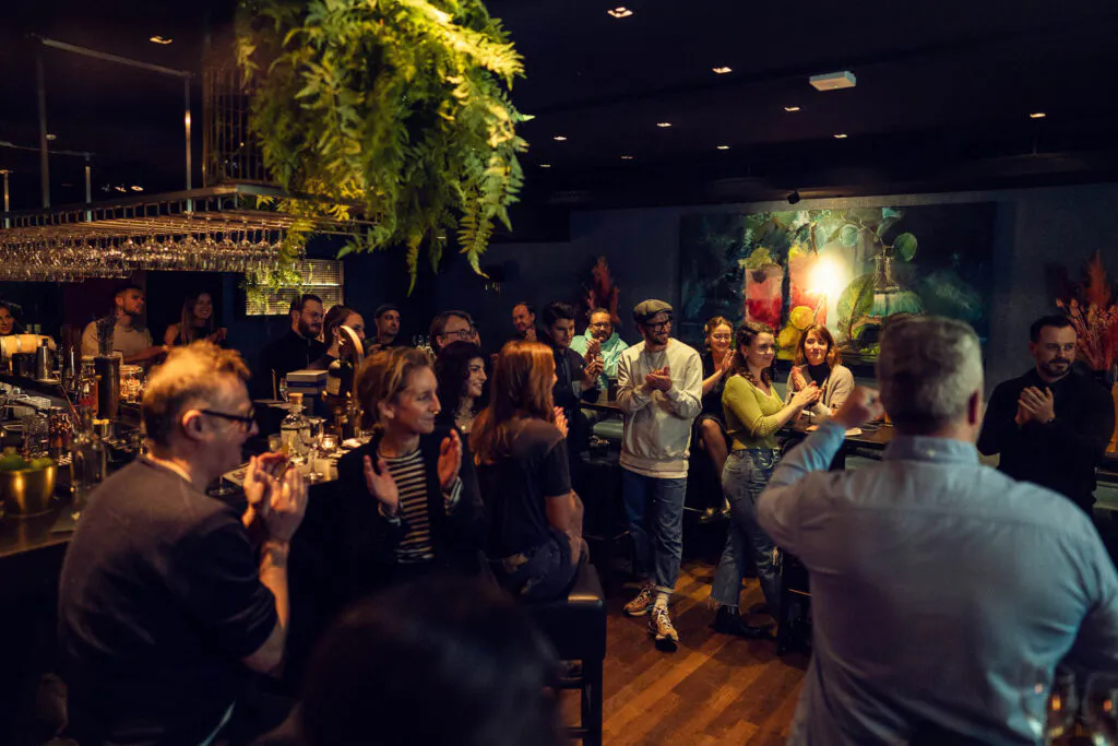 Gäste stehen und sitzen bei einem Botucal-Rum-Event in einer dunkel beleuchteten Bar mit Hängepflanzen und Gläserregal.