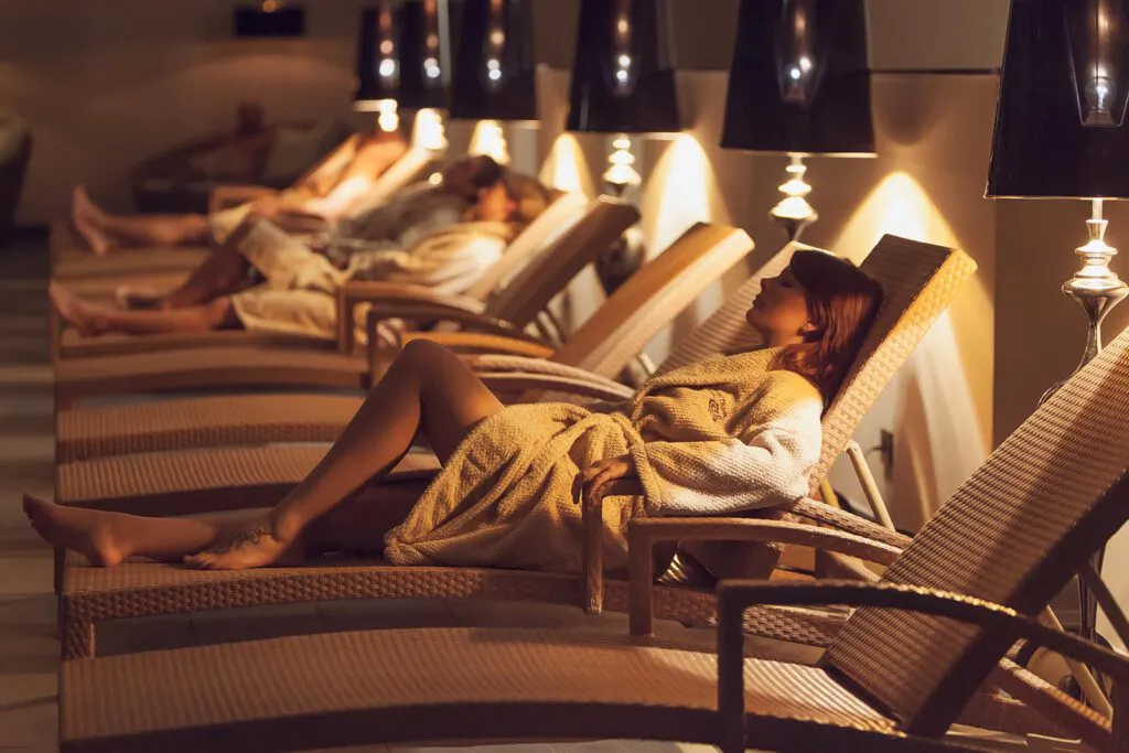 Gäste in Bademänteln entspannen auf Korbliegen im warm beleuchteten Ruheraum der VitaSol Therme.