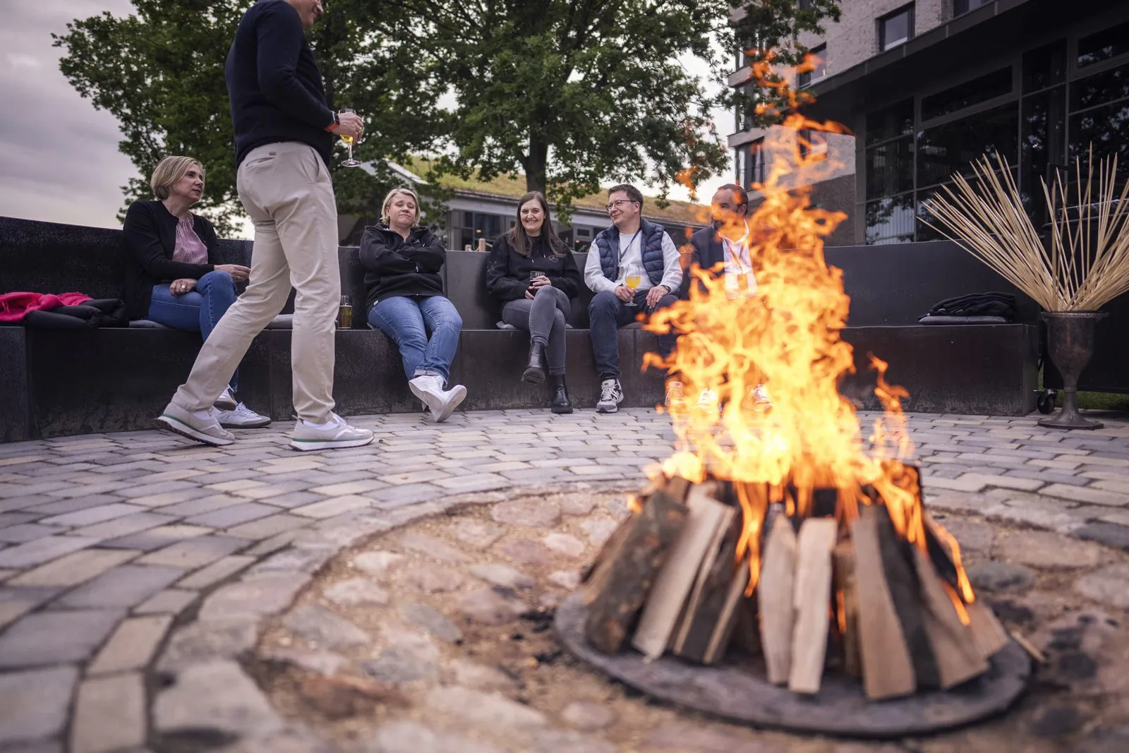Gäste sitzen im gepflasterten Innenhof um ein loderndes Holzfeuer, ein Mann geht daran vorbei.