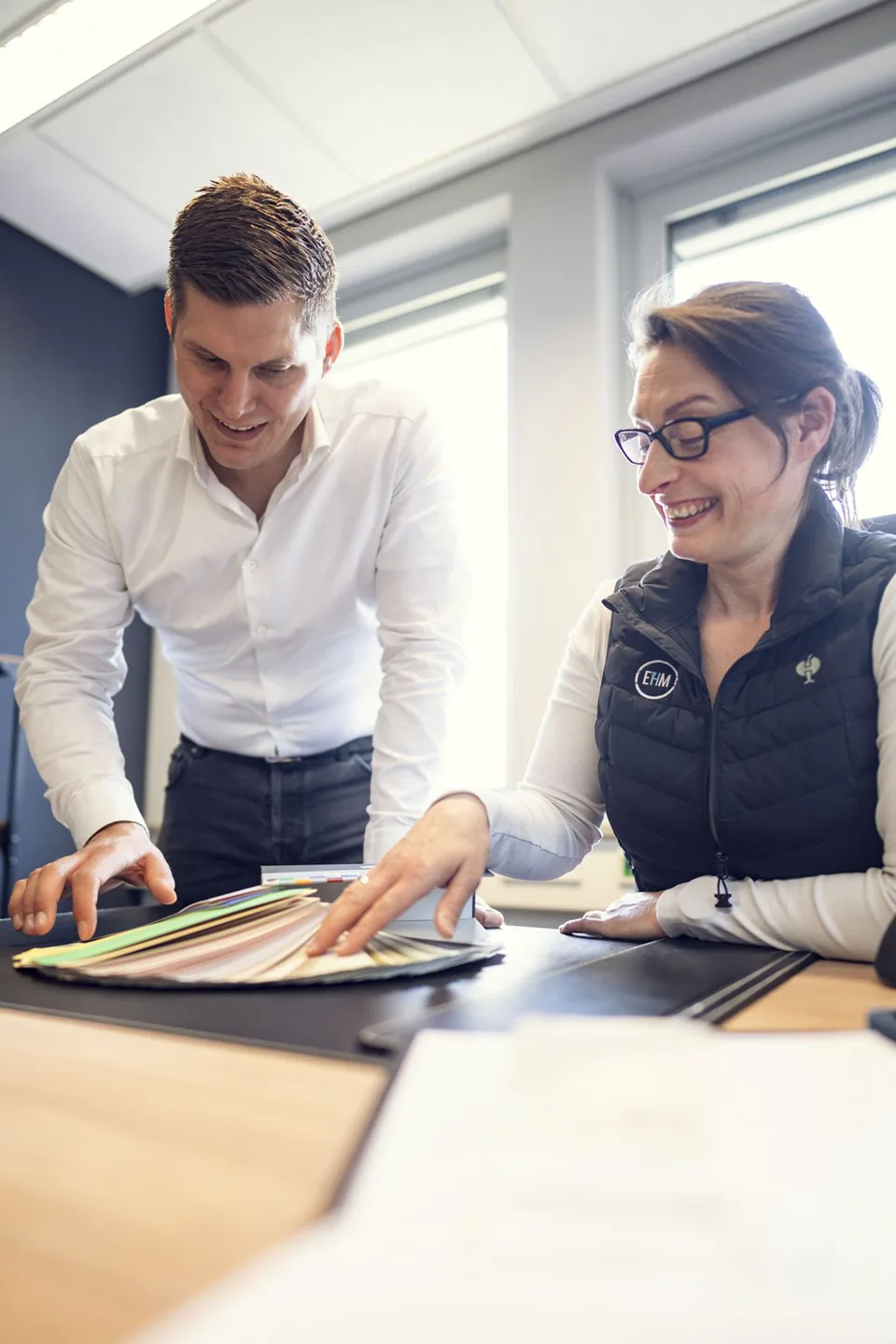 Mann und Frau sichten Materialmuster auf einem Tisch im hellen Büro von Elb Handwerk.