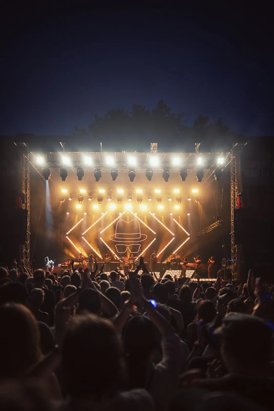 Publikum mit erhobenen Armen vor der goldgelb beleuchteten Open-Air-Bühne beim Konzert von Jan Delay.