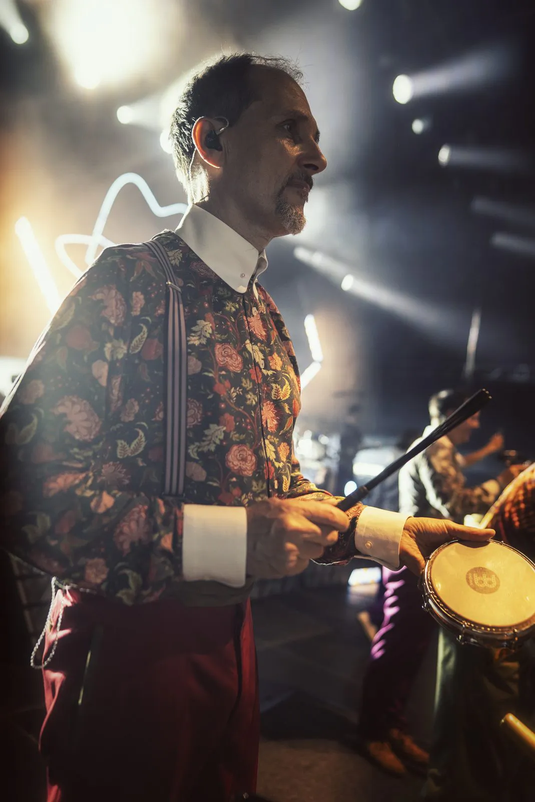 Perkussionist im Blumenhemd mit Hosenträgern spielt eine Trommel im hellen Gegenlicht auf der Konzertbühne.