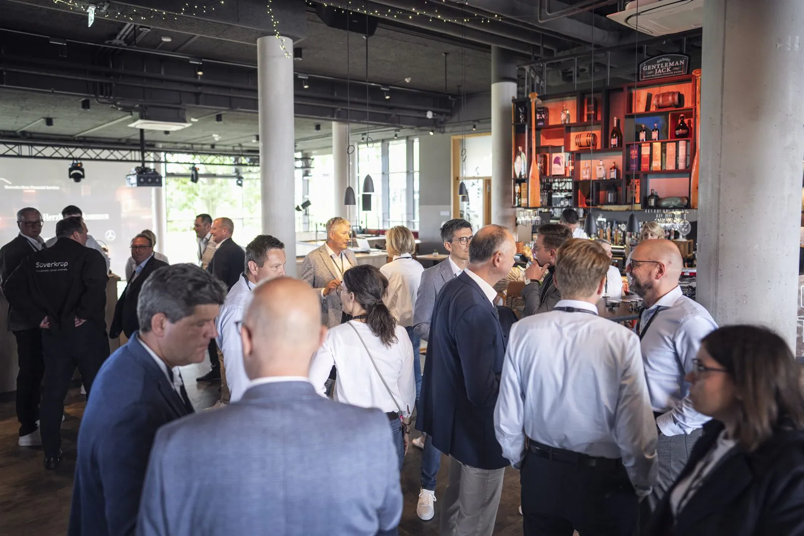 Gäste in Businesskleidung unterhalten sich bei Tageslicht vor einer Bar beim Mercedes-Benz-Event.