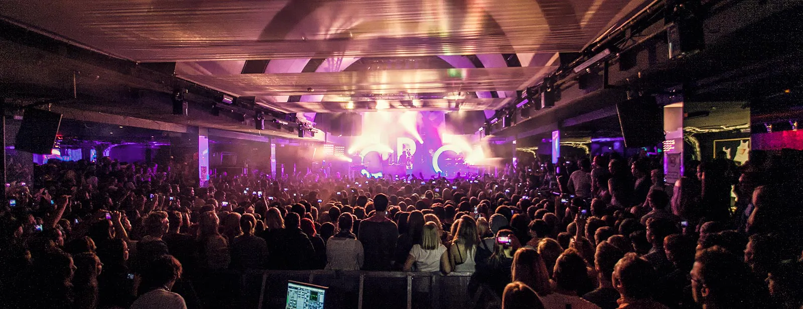 Dichtes Publikum vor der Bühne beim CRO-Konzert in einer Halle mit violettem und gelbem Scheinwerferlicht.