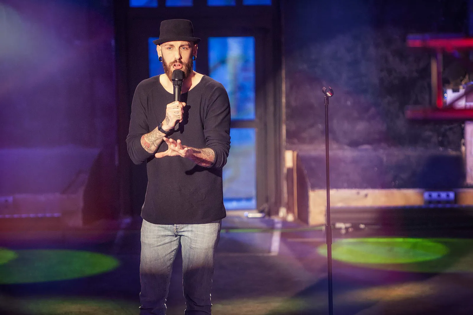 Dennis Grundt mit Hut und Mikrofon auf der Bühne des NDR Comedy Contests im violetten und grünen Licht.