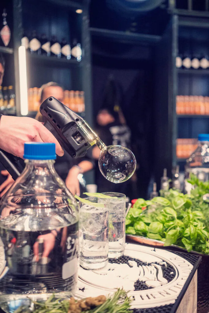 An der Eventbar entsteht mit einem Handgerät eine Rauchblase über Drinks mit Eis, Limette und Kräutern.
