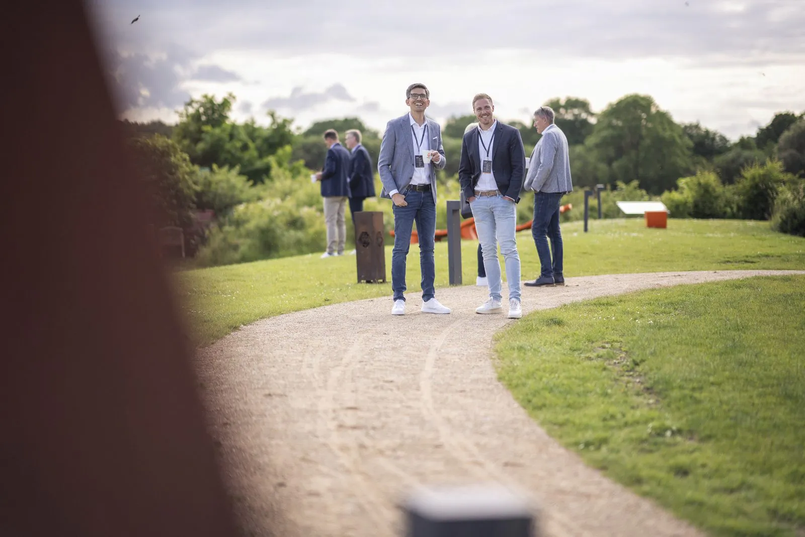 Mehrere Männer mit Namensbändern stehen auf einem Kiesweg im Grünen bei Tageslicht.