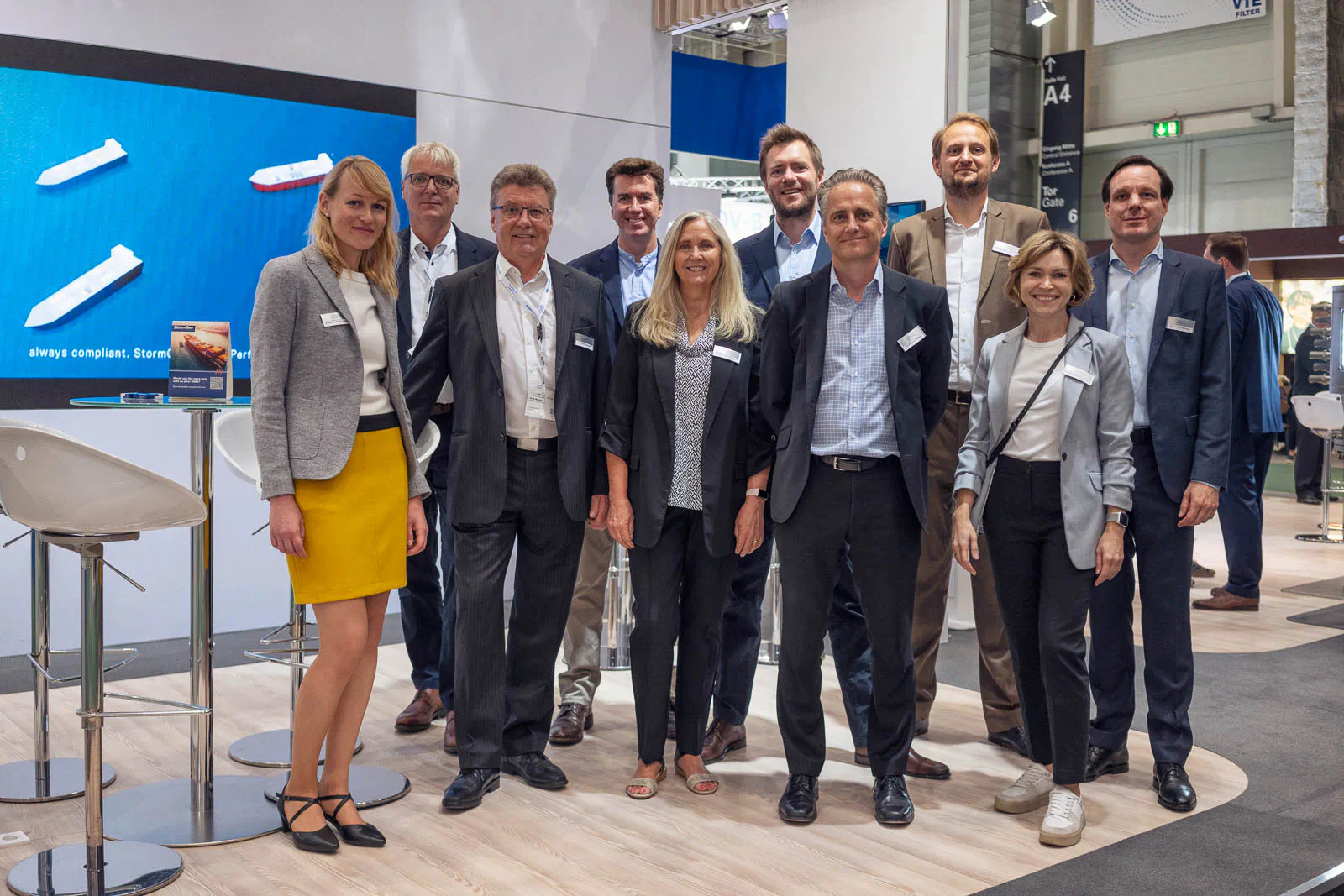 Gruppe in Geschäftskleidung posiert am hell beleuchteten Alfa-Laval-Messestand vor einem Bildschirm.