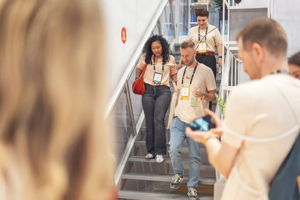 Personen mit Messeausweisen gehen eine Treppe am Awin-Messestand hinunter, vorne hält ein Mann ein Smartphone.
