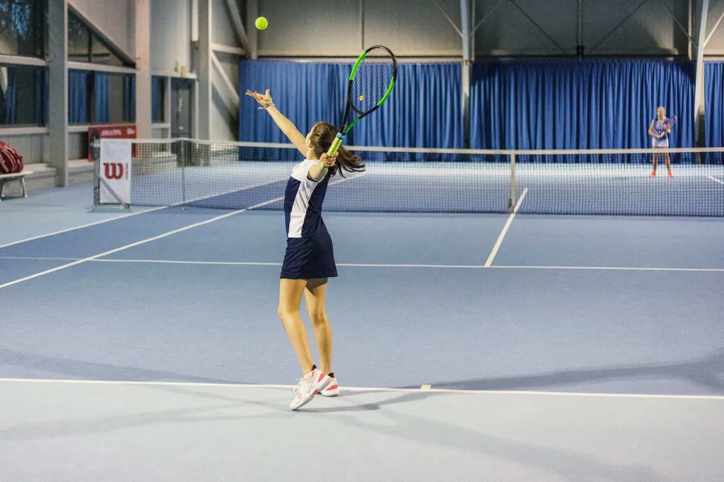 Tennisspielerin beim Aufschlag auf blauem Hallenplatz, Gegnerin hinter dem Netz beim Wilson Master Cup.