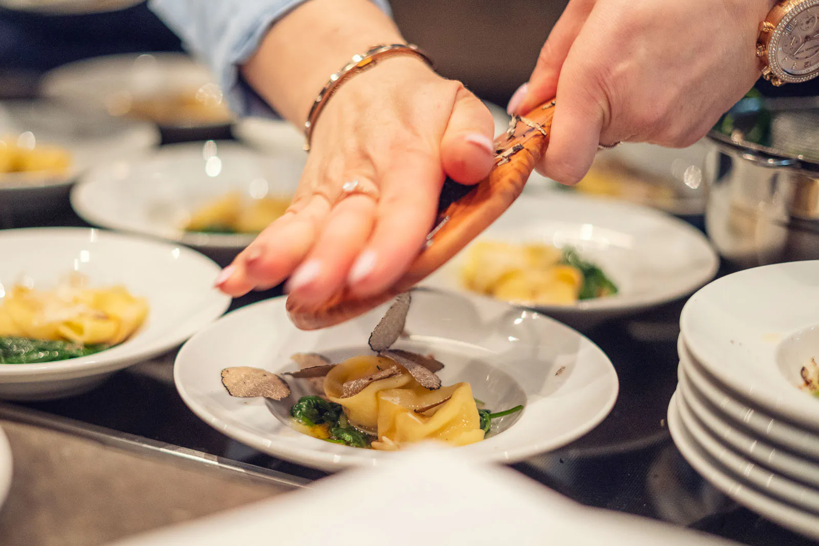 Hände richten gefüllte Pasta mit Trüffelscheiben und grünem Gemüse auf weißen Tellern an.