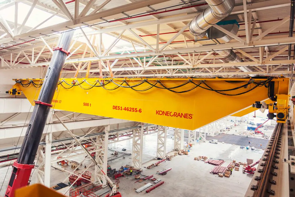 Gelber Konecranes-Brückenkran mit 500-Tonnen-Markierung in einer hellen Industriehalle mit Stahlträgern.