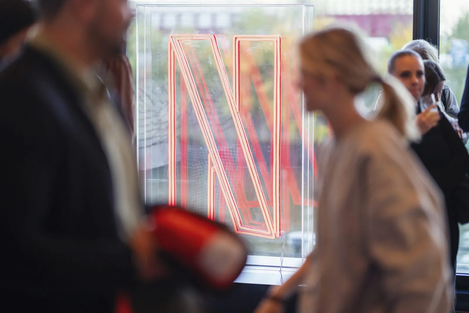 Gäste vor einem rot leuchtenden Netflix-N in einem transparenten Schaukasten am Fenster.