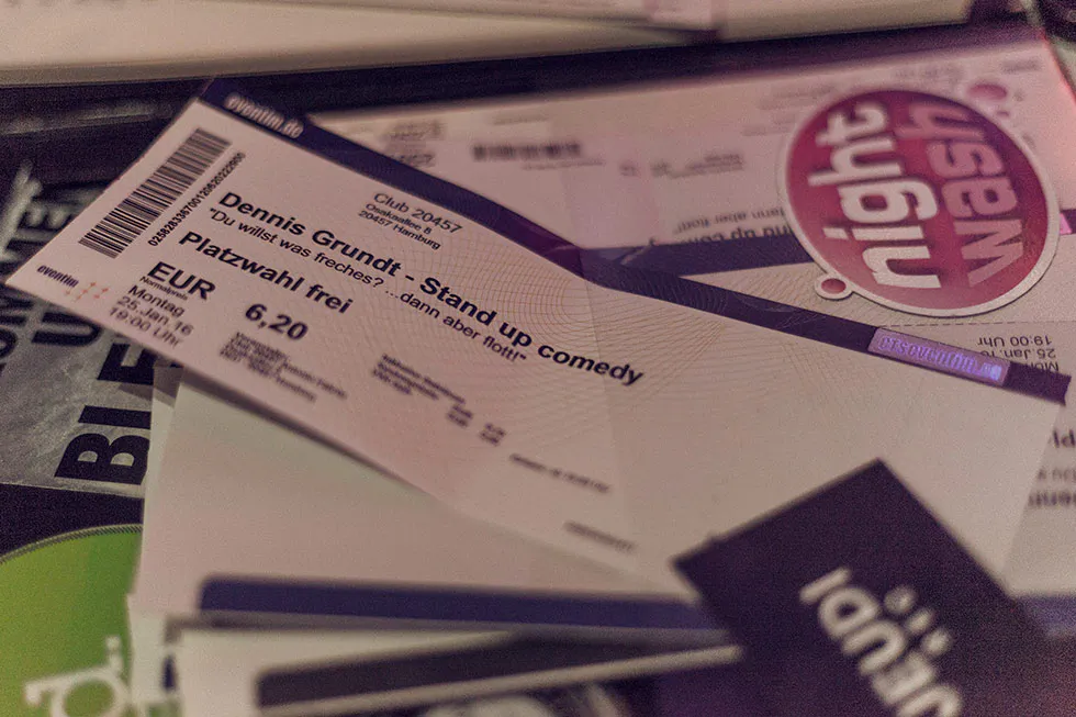 Eintrittskarte für Dennis Grundts Stand-up-Comedy mit freier Platzwahl liegt auf Flyern und weiteren Tickets.
