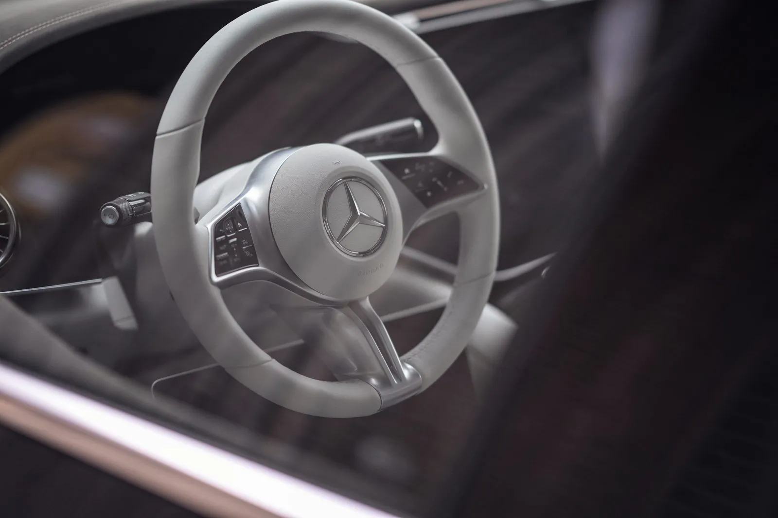 Helles Mercedes-Benz-Lenkrad mit Stern und Bedientasten, durch die spiegelnde Seitenscheibe im dunklen Innenraum gesehen.