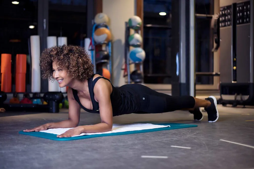 Marie Amière hält lächelnd einen Unterarmstütz auf einer Matte im Fitnessraum des Aspria Uhlenhorst.