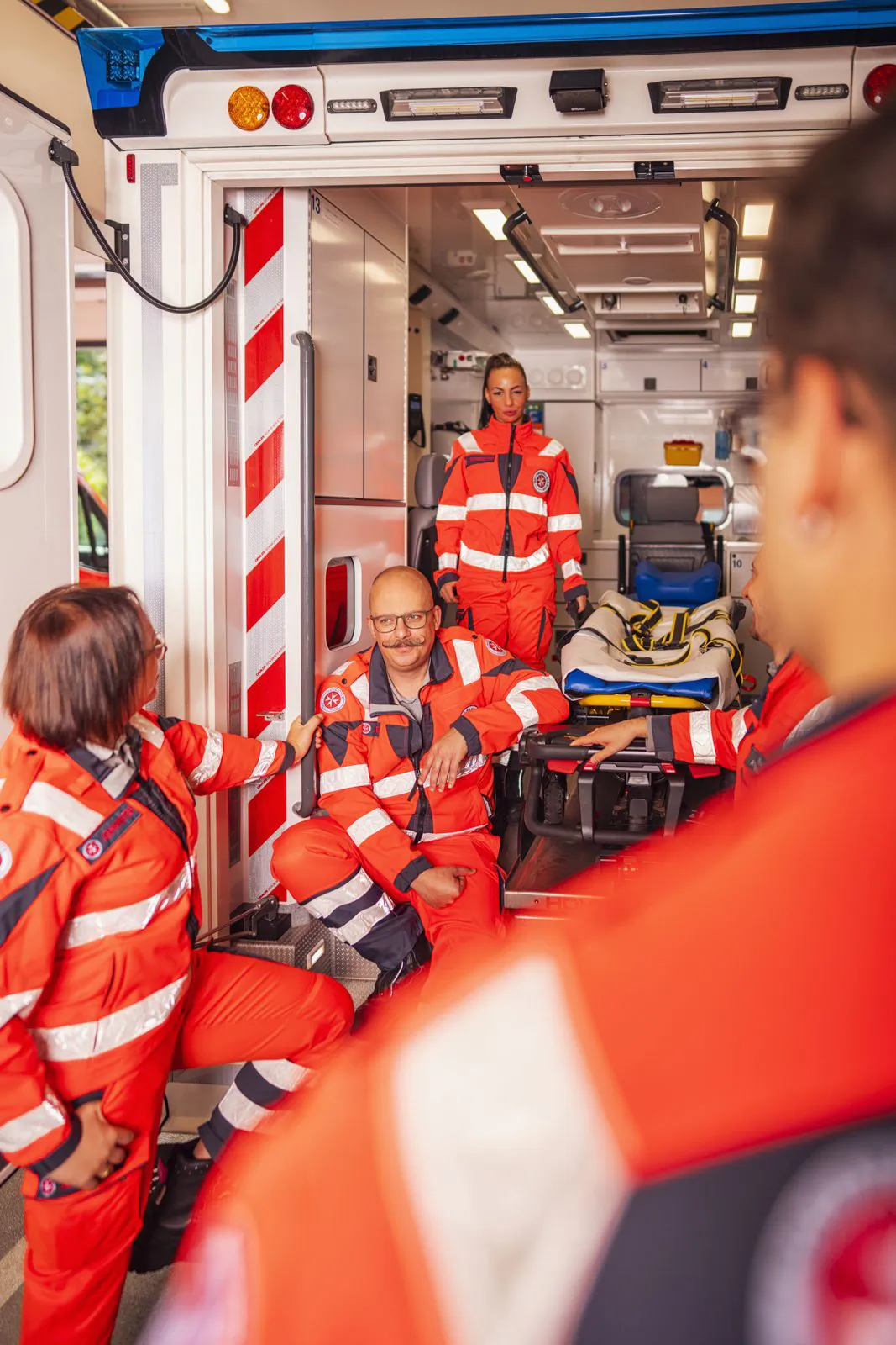 Johanniter-Rettungskräfte in rot-weißer Einsatzkleidung sitzen und stehen am offenen Heck eines Rettungswagens.