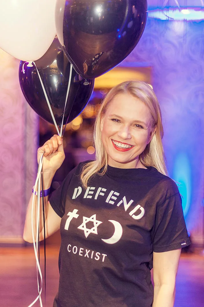 Lächelnde Frau im schwarzen T-Shirt hält schwarze und weiße Luftballons bei violett-blauer Eventbeleuchtung.