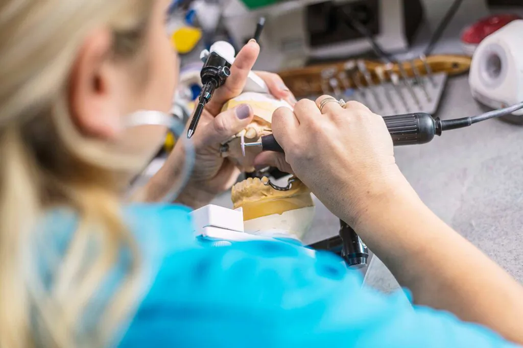 Person bearbeitet ein Gebissmodell mit einem Handstück am beleuchteten Arbeitsplatz im Dental-Labor Ralf Gaida.
