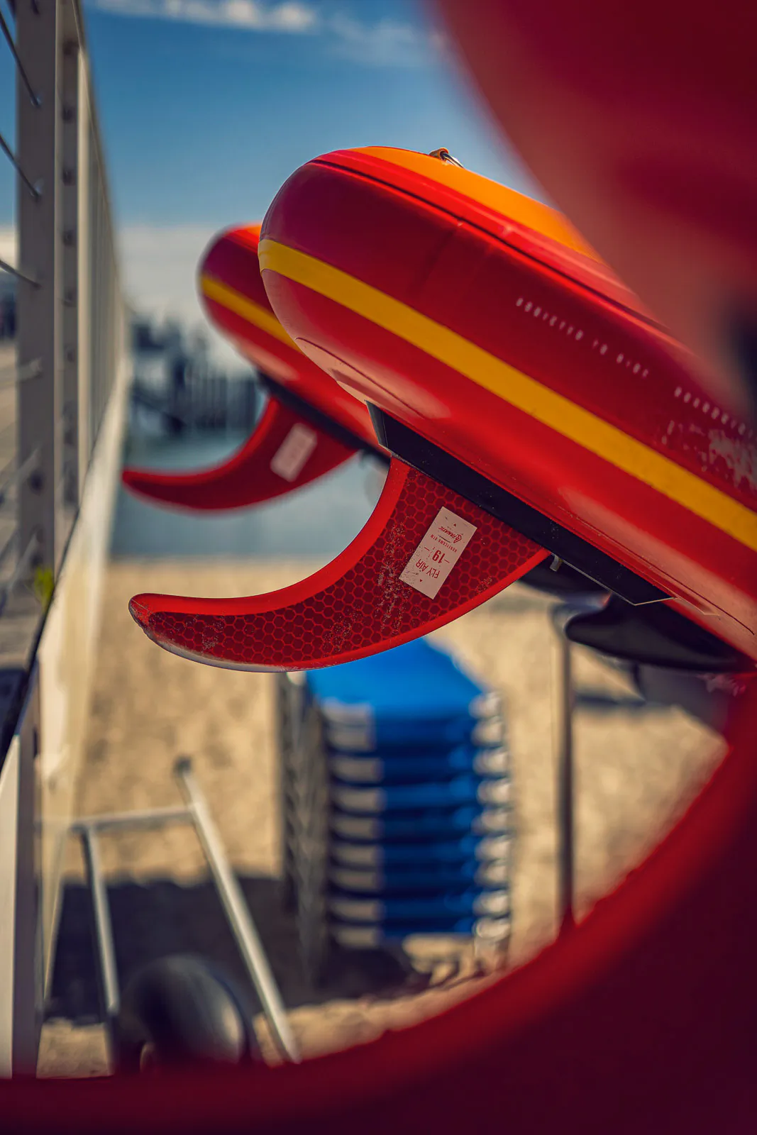 Rote Stand-up-Paddle-Boards mit gelben Streifen und Finnen lagern im Sonnenlicht an einer Strandstation.