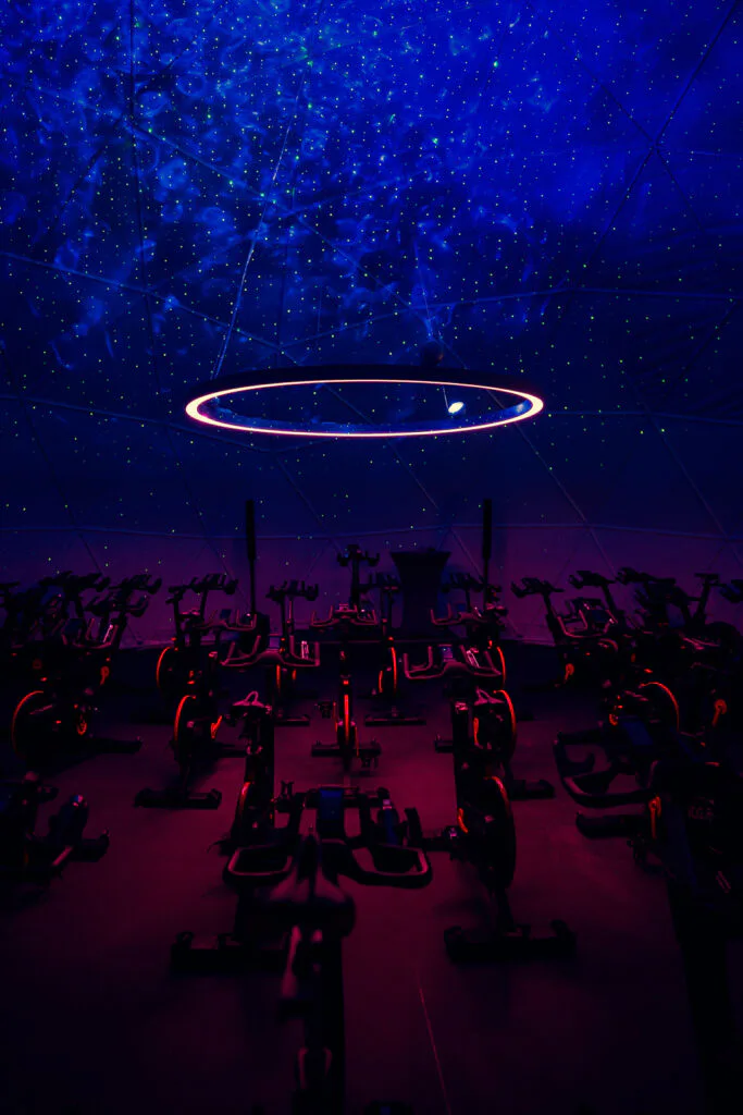 Indoor-Cycling-Raum mit Spinningrädern, blauem Sternenlicht an der Decke und pink leuchtendem Lichtring.